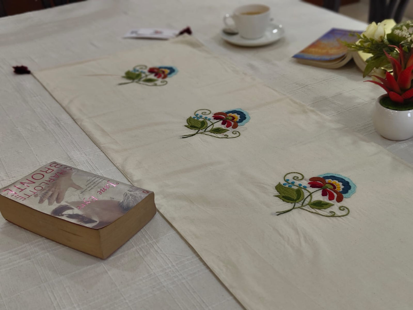 Tablecloth with floral embroidery on a table with a book and cup.