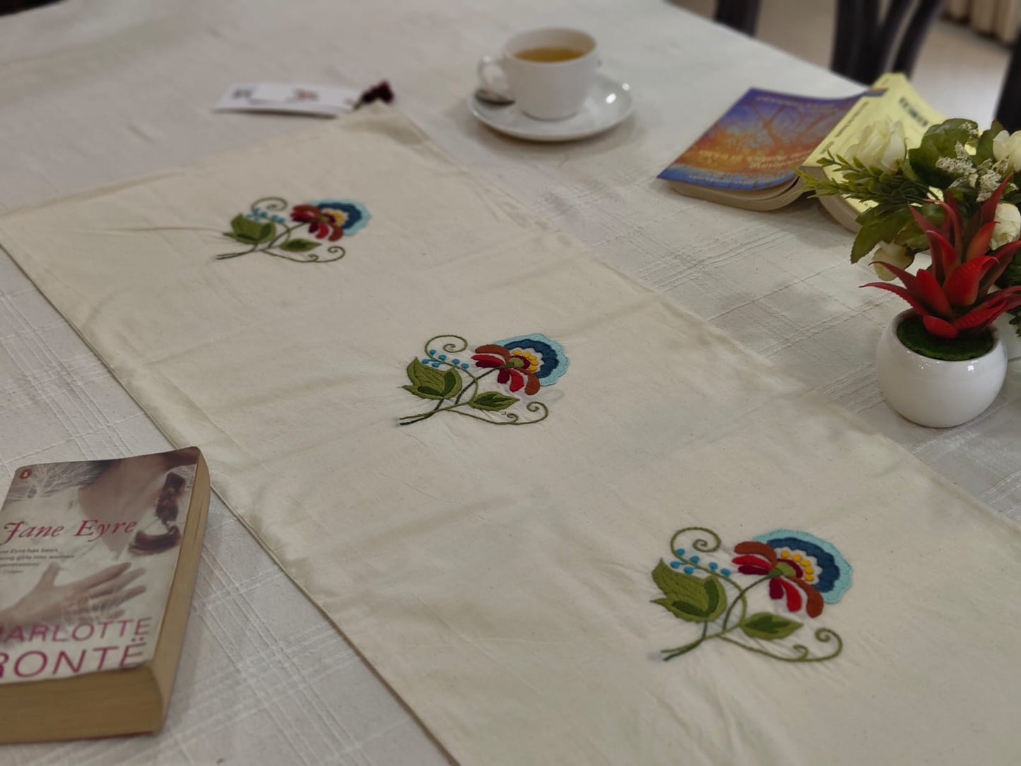 Table setting with embroidered tablecloth, books, and a cup of tea.