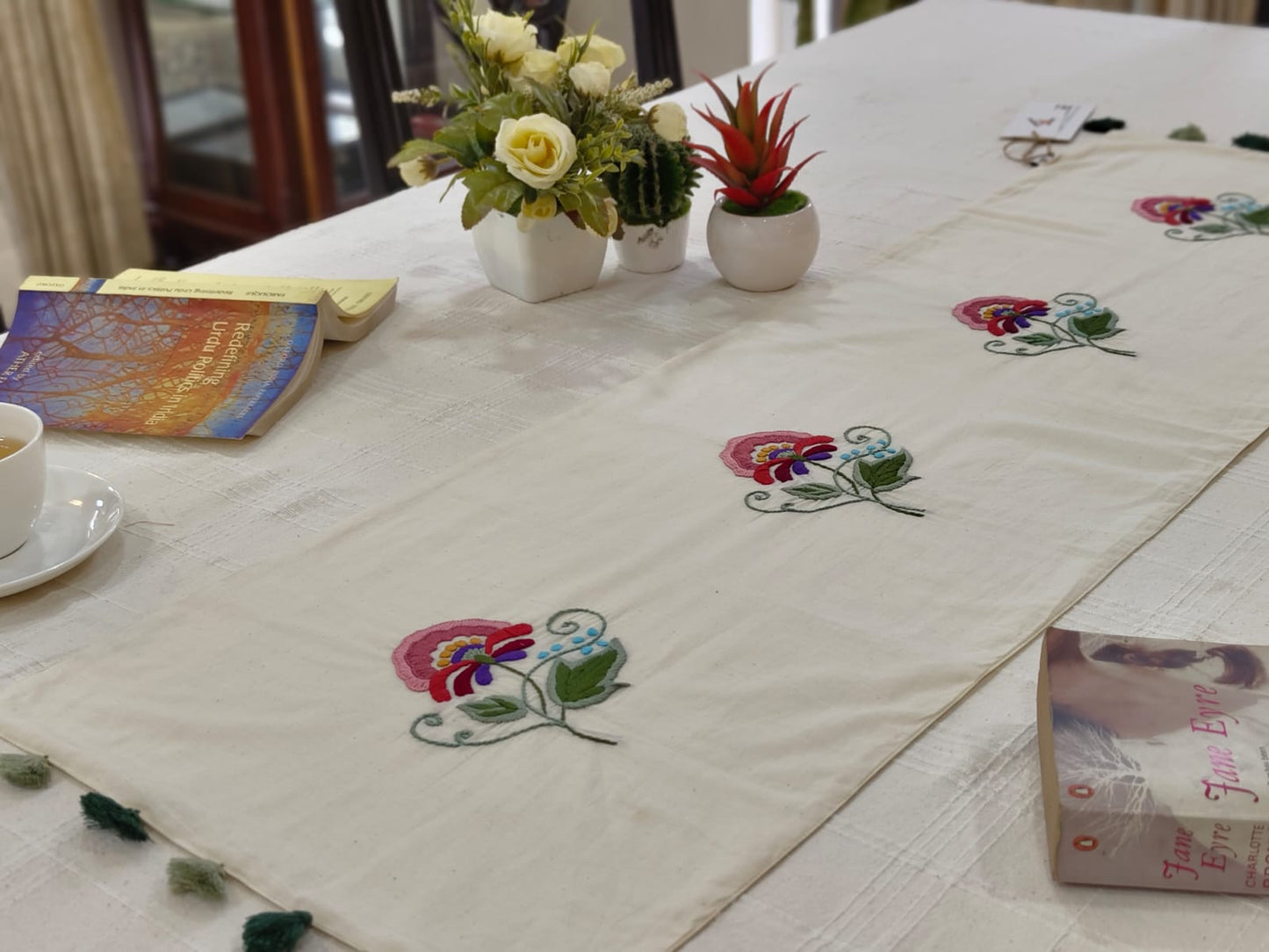 Table setting with embroidered table runner, flowers, and books on a light surface.